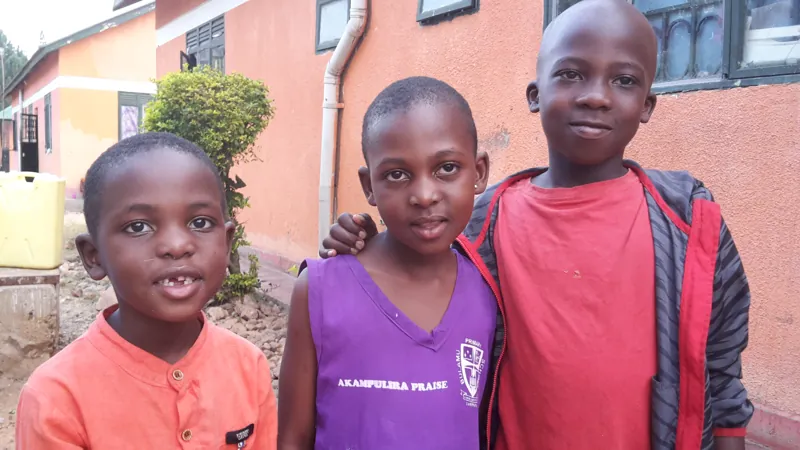 Drie kinderen voor een van de huizen op Bulamu